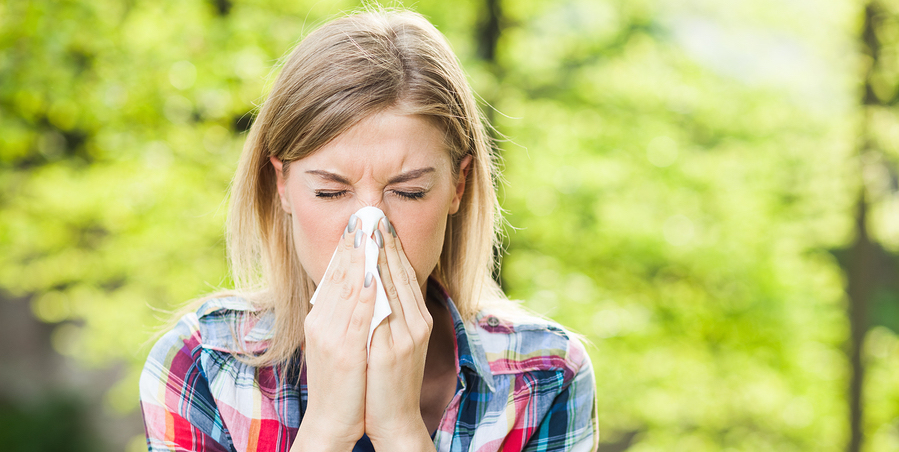 blonde woman outside sneezing due to allergies