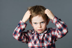 young boy with freckles scratching his hair for head lice