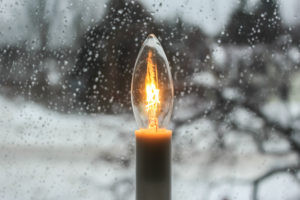 Shining lightbulb in front of raindrop covered window with a winter backdrop